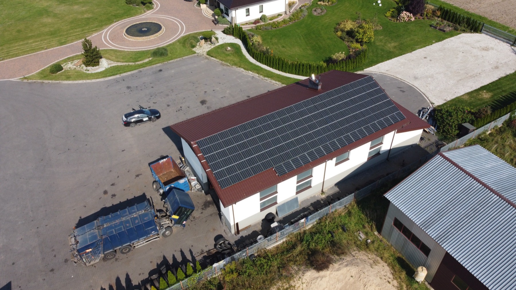 Instalacja fotowoltaiczna na dachu budynku wśród zabudowy, widok z drona